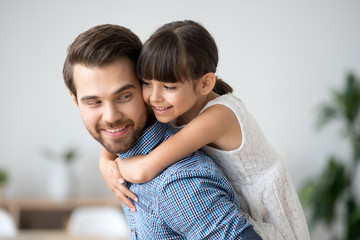 Cute girl embracing dad carrying child on back, little daughter hugging father having fun at home,...