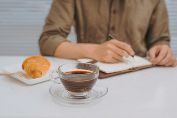 man's hand wrote message on white notebook with pen and croissant on wood table, business vintage concept
