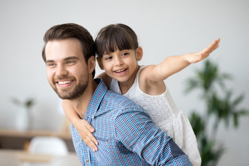 Carefree active child enjoying dad piggybacking cute daughter playing on weekend, happy father...