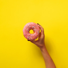 Woman hand holding delicious pink donut on yellow color background. Top view banner with copy...