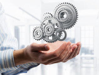 Engine mechanism in male ahnds as symbol for cooperation or teamworking. Mixed media