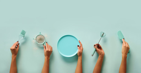 Female hands holding kitchen tools, sieve, rolling pin, plate, sieve, brush, whisk, spatula for baking and cooking over pastel blue background. Food frame, bake concept with copy space