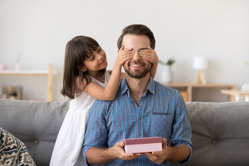 Cute kid daughter making surprise to smiling dad receiving gift box on fathers day, little child...