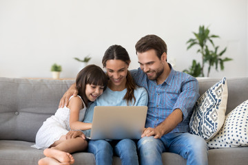 Happy family with kid girl having fun using laptop together sitting on sofa, parents and child...