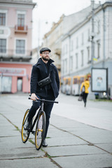 A young stylish bearded businessman pushing a bicycle while going to work.