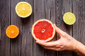 Bright citrus fruits on a wooden dark background. Female hand holds grapefruit.