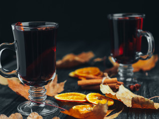 Hot drink mulled wine on a wooden table with autumn leaves, cinnamon and citrus