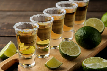 gold tequila in a glass shot glass with salt and lime on a brown wooden background. bar. alcoholic...