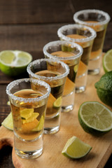gold tequila in a glass shot glass with salt and lime on a brown wooden background. bar. alcoholic...