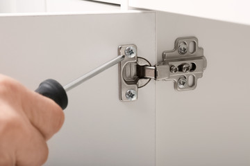 Man fixing door of white wardrobe with screwdriver, closeup