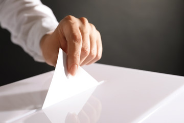 Woman putting her vote into ballot box on black background, closeup