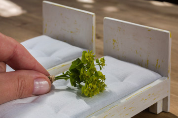 Woman's hand putting a bouquet of yellow flowers on a miniature bed, two small wooden beds with white mattress, doll house furniture, home decoration