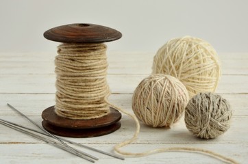 Wool balls and spool with yarn thread on white wooden background close-up.