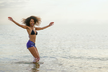 afro hair girl jumping in the sea on beach vacation. concept of woman freedom happy single.