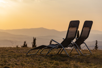 Two empty chaise lounges on a grass overlooking the hills of Tuscany in evening light, Italy