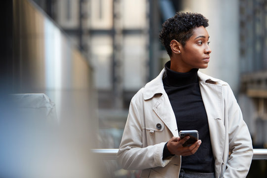 Young black businesswoman standing in the city with smartphone in hand, close up, selective focus