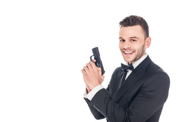 cheerful secret agent in black suit holding gun, isolated on white