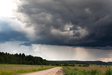 The dirt road through the field leading to the thunderstorm clouds