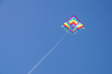 angle view of a colorful kite flying with waving red bow in a deep blue sky with the light of the sun