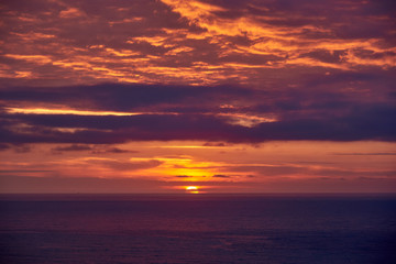 Obraz na płótnie Canvas Seashore with violet water and orange purple sky.