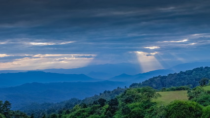 sunset at Huai Nam Dang National Park, mountain view evening of dark clouds moving above many hill around with soft mist and sun rays in the sky background, Huai Nam Dang, Chiang Mai, Thailand.