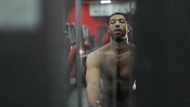 Young afro-american man performs an exercise on the simulator.