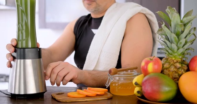 Adult Man Making Green Juice With Juice Machine In Home Kitchen After A Workout.