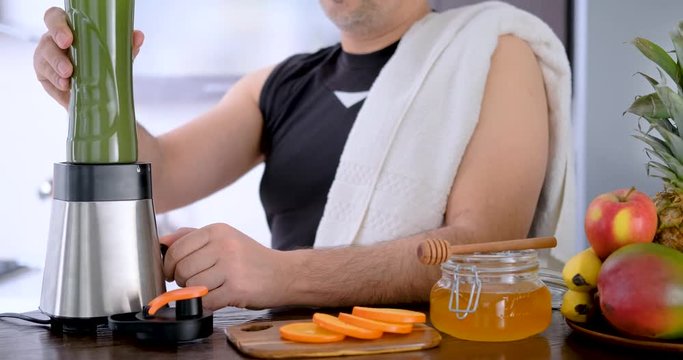 Adult man making green juice with juice machine in home kitchen after a workout.