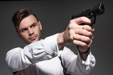 handsome secret agent aiming with handgun isolated on grey