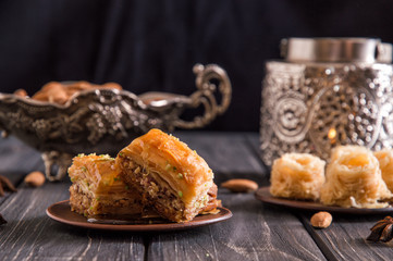 Close up. Eastern still life. Turkish traditional honey baklava, nuts. Pottery and silverware. Dark wooden background.