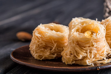 Close up, macro. Eastern sweets on an old clay saucer. Turkish traditional Baklava bird's nest. Dark wooden background.