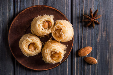 Top view, flat lay. Close up. Turkish traditional sweets on an old clay saucer. Baklava bird's nest. Dark wooden background.