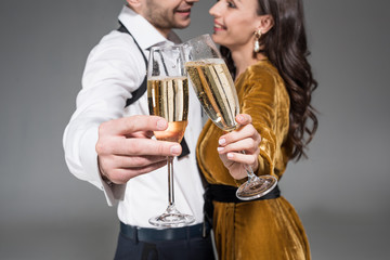 selective focus of couple clinking with champagne glasses isolated on grey