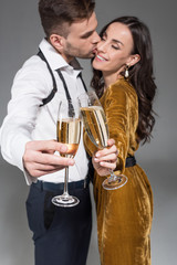 selective focus of kissing couple clinking with champagne glasses isolated on grey