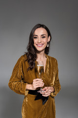 Fototapeta premium portrait of attractive elegant smiling woman in golden dress holding glass of champagne isolated on grey