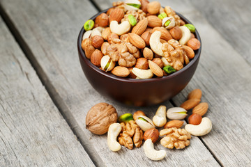 Wooden bowl with mixed nuts on a wooden gray background. Walnut, pistachios, almonds, hazelnuts and cashews, walnut.