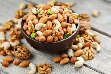 Wooden bowl with mixed nuts on a wooden gray background. Walnut, pistachios, almonds, hazelnuts and cashews, walnut.