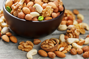 Wooden bowl with mixed nuts on a wooden gray background. Walnut, pistachios, almonds, hazelnuts and cashews, walnut.