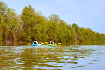 Fototapeta na wymiar Two women paddle in yellow and blue kayaks on the Danube river at spring. Water tourism and recreational at spring