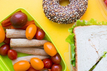 School lunch box. Sandwich, a banana, candies, baby corns, carrot and tomatoes in green plastic container