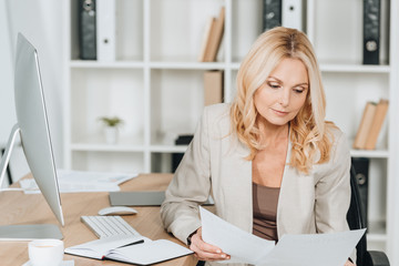 concentrated professional businesswoman sitting and working with papers in office