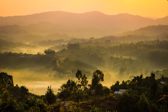 Gentle yellow light and light mist over the hills in country side with traditional houses and the tropical nature of Uganda on the border with the Congo at dawn