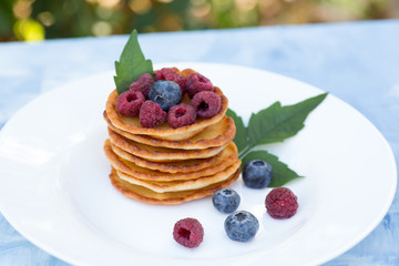 A stack of delicious pancakes with sour cream, raspberries and blueberries on a light background. with copy space