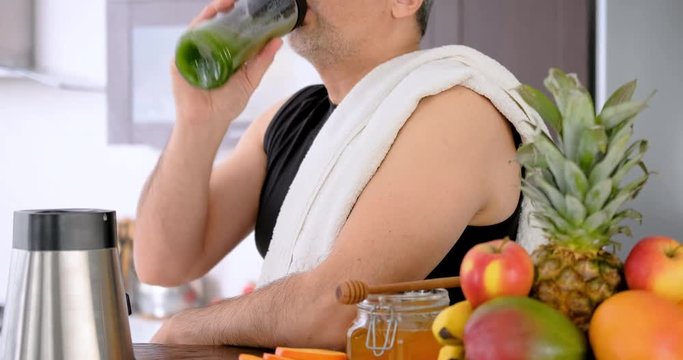 Adult man drinking smoothie in home kitchen after a workout.