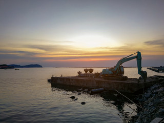 Fototapeta na wymiar Excavator Working construction bridge In the sea During the time of sunset.