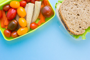 School lunch box. Bread, candies, baby corns, carrot and tomatoes in green plastic container