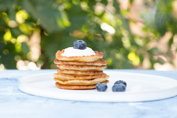 A stack of delicious pancakes with sour cream, raspberries and blueberries on a light background....