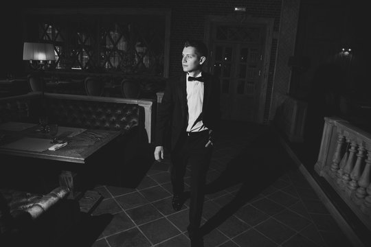 Photos of elegant young man in suit and bowtie walking around the restaurant, looking to the side, black and white photo