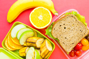 School lunch box. Bread, orange, baby corns, carrot and tomatoes in green plastic container