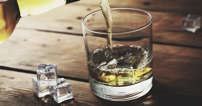 pouring whiskey from bottle into a glass with ice cubes